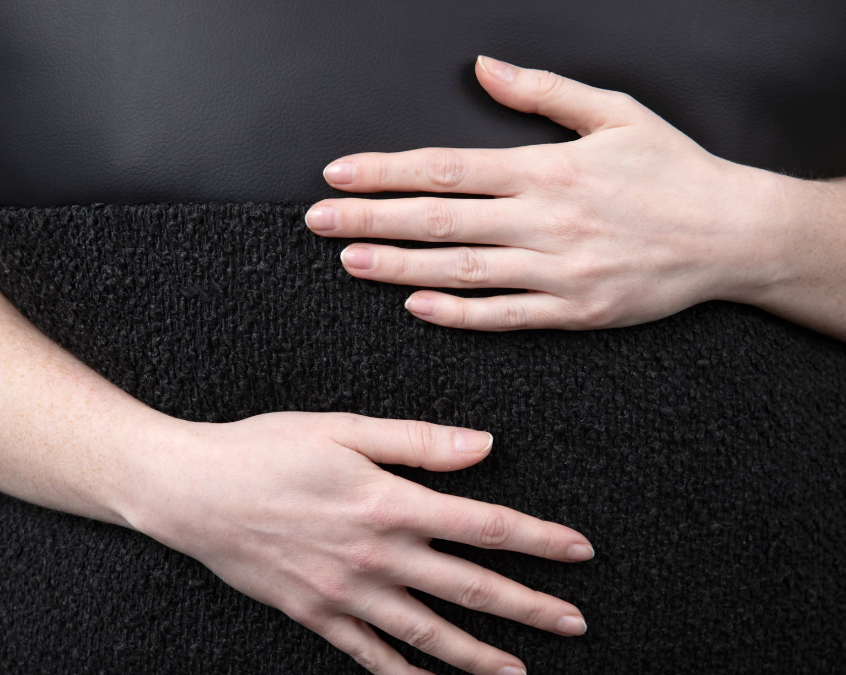 Hands touching the looped texture of a black bouclé decorative pillow cover — close-up fabric detail showing the dimensional curled yarn surface of a black bouclé throw pillow by Coterie Brooklyn