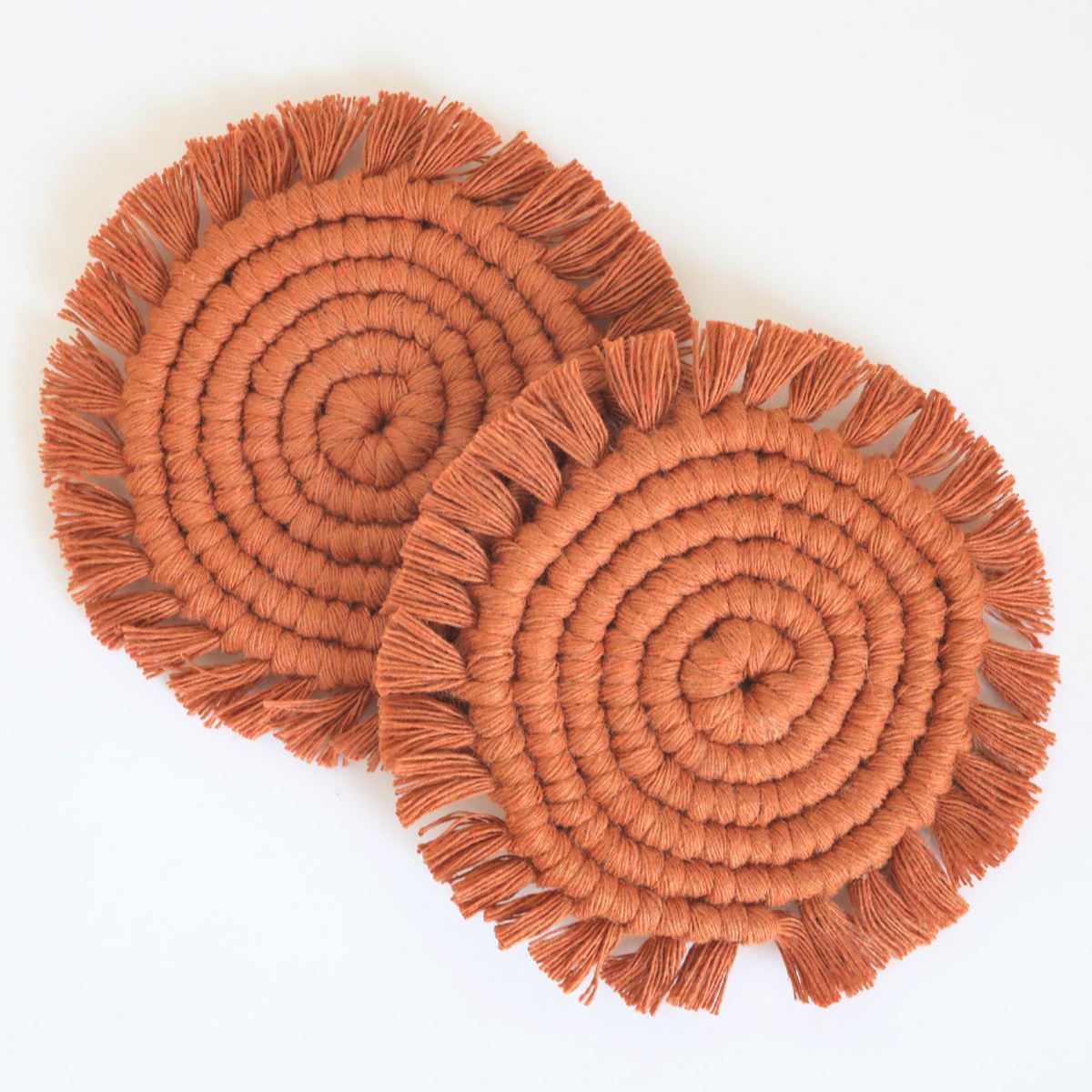 Set of two terracotta macrame coasters with fringe edges overlapping, flat lay