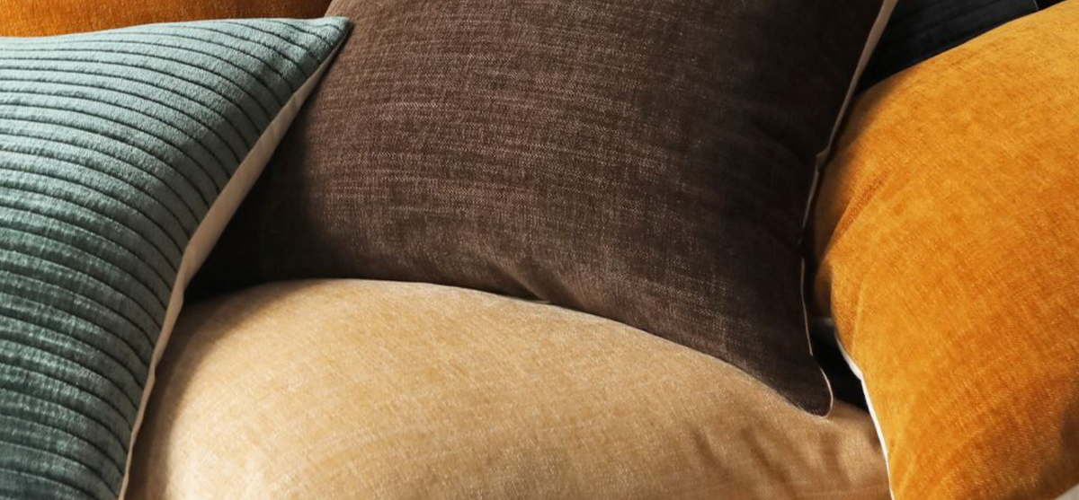 Close-up of mustard, brown, sage, and blue velvet throw pillows layered together
