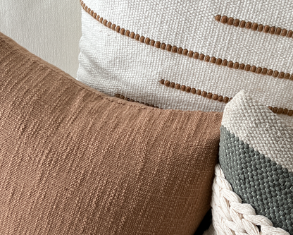 Close up of sepia cotton pillow cover layered with stripe and cream textured pillow covers