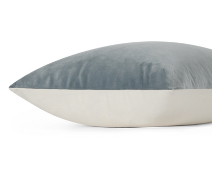 A close-up of a rectangular throw pillow with a slate blue velvet top half and a cream fabric bottom half, shown against a plain white background.