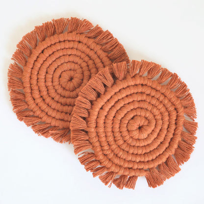 Set of two terracotta macrame coasters with fringe edges overlapping, flat lay